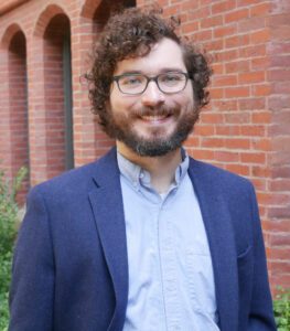 A man with curly hair and a beard smiles at the camera