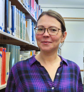 Olga Makarova is a woman with glasses wearing a purple shirt