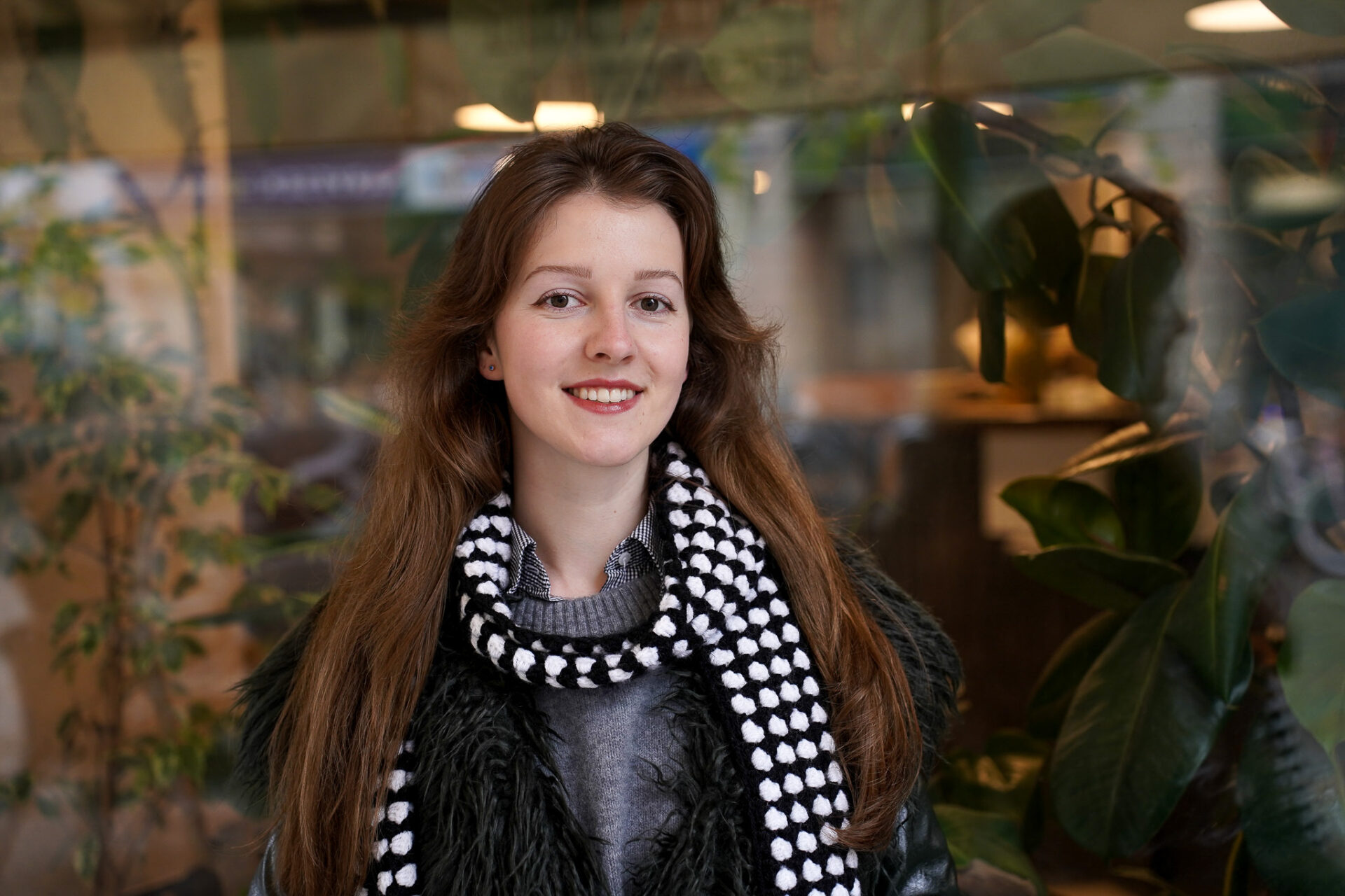 A smiling woman wearing a black jacket and a checkered scarf