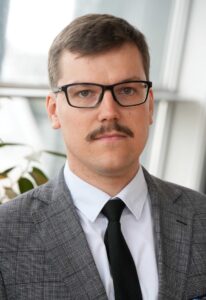 A man with glasses and a mustache in a gray suit