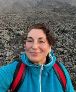 A smiling woman in a blue jacket on top of a volcano